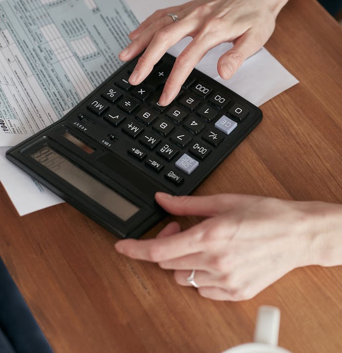 Person calculating finances with a calculator and document on a wooden desk.